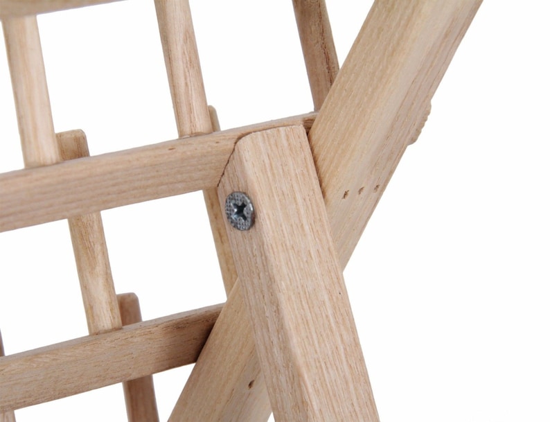 May include: Close-up of a wooden easel with a screw connecting the legs. The easel is made of natural wood and has a light brown color.