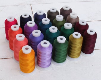 May include: A collection of 20 spools of embroidery thread in various colors, including red, orange, yellow, green, blue, purple, brown, and burgundy. The spools are arranged in a triangular shape on a white wooden surface.