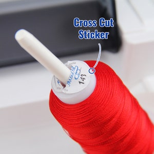 May include: A spool of red thread with a white label that says "Janlynn" and "143". The label also has a cross cut sticker that says "Cross Cut Sticker".