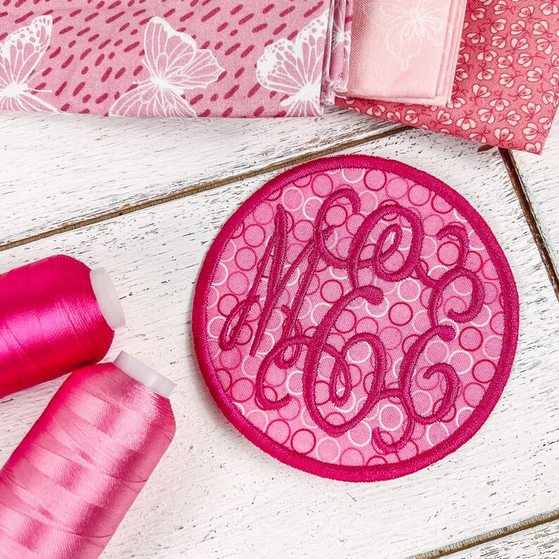 a pink circle with a monogrammed mono on it next to two spool