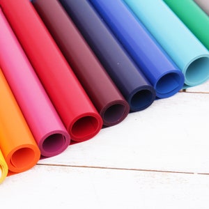 May include: A collection of colorful rolls of paper, arranged in a rainbow pattern, with the ends of the rolls facing the viewer. The rolls are on a white wooden surface.