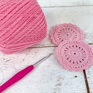 a pink crochet doily next to a pink crochet hook