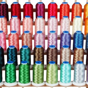 May include: A collection of 48 spools of thread in various colors, arranged on a wooden rack. The spools are all the same size and shape, and they are wound with different colors of thread.