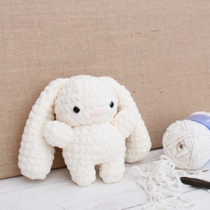 May include: A white crocheted bunny rabbit toy with long floppy ears. The bunny has black eyes and a pink nose.