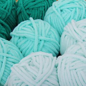 May include: A close-up of several balls of yarn in shades of green and blue. The yarn is soft and fluffy, and it is perfect for knitting or crocheting.