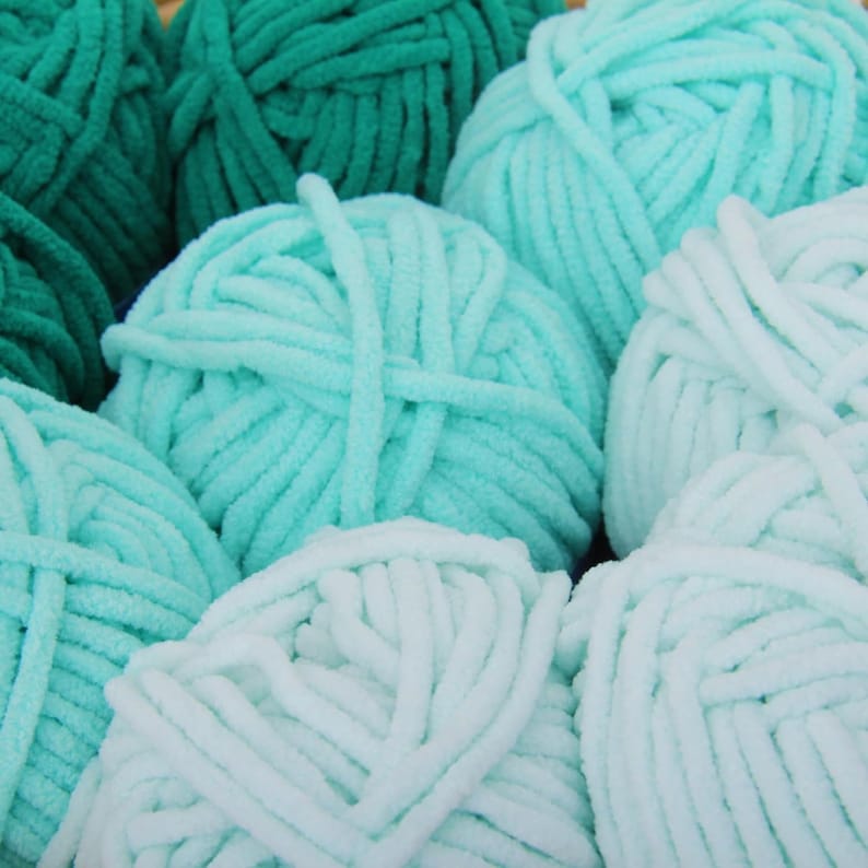 May include: A close-up of several balls of yarn in shades of green and blue. The yarn is soft and fluffy, and it is perfect for knitting or crocheting.