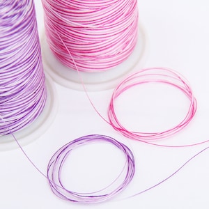 May include: Two spools of embroidery floss, one pink and white, the other purple and white. The floss is wound around the spools and is ready to be used for embroidery projects.