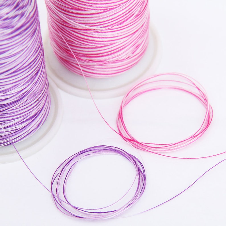 May include: Two spools of embroidery floss, one pink and white, the other purple and white. The floss is wound around the spools and is ready to be used for embroidery projects.