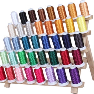 May include: A wooden thread rack with five tiers holds 48 spools of embroidery floss in a variety of colors, including white, beige, blue, green, red, pink, purple, and yellow.