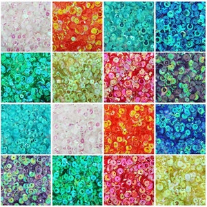May include: Assortment of 12 different colors of iridescent sequins. Each color is displayed in a square section. The colors include white, red, blue, green, purple, and yellow.