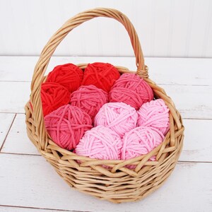 May include: A wicker basket filled with balls of yarn in shades of pink and red. The yarn is arranged in a gradient from red to pink.