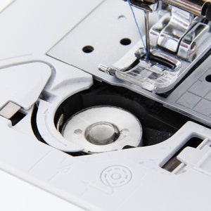 May include: Close-up of a white sewing machine with a bobbin winder and a needle threaded with blue thread.