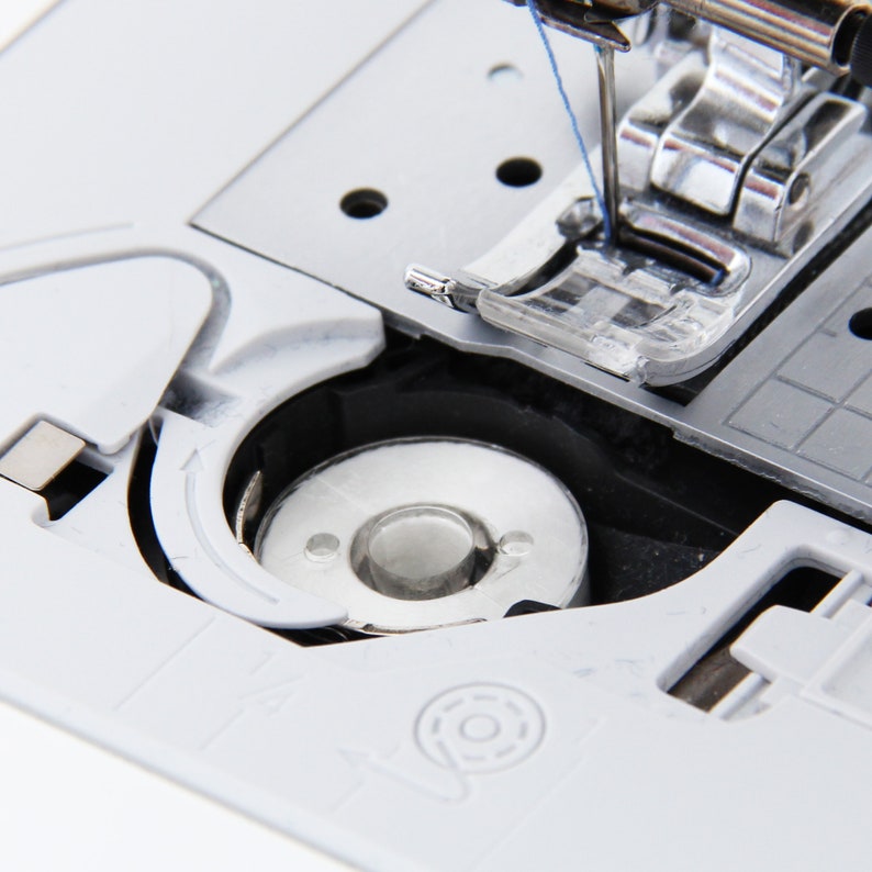 May include: Close-up of a white sewing machine with a bobbin winder and a needle threaded with blue thread.