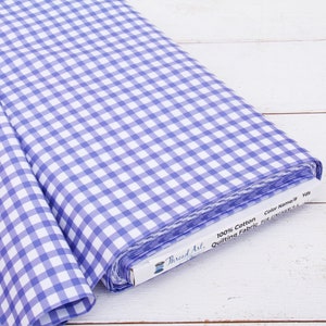 May include: A roll of blue and white gingham fabric. The fabric is 100% cotton and is labeled as quilting fabric. The fabric is on a white wooden surface. The label reads "Thread Art".