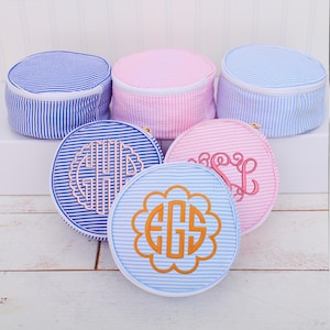May include: Five round, zippered cosmetic bags and matching hat boxes in blue and pink seersucker fabric. The bags feature embroidered monograms in coordinating colors. The hat boxes have white zippers.
