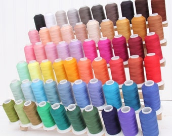 May include: A rainbow assortment of thread spools organized on a wooden rack. The spools are arranged in rows, with each row featuring a different color. The colors include red, orange, yellow, green, blue, indigo, and violet.
