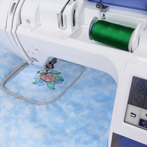 May include: A white embroidery machine with a green thread spool and a hoop with a blue and orange embroidered turtle design.