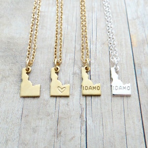 May include: Three gold necklaces with Idaho state outline pendants. One pendant has a small heart, one says "IDAHO", and one says "IDAHO" in a smaller font.
