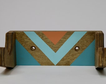 Könnte beinhalten: Eine Wandhalterung aus Holz mit zwei Haken, die in einem geometrischen Muster aus Türkis, Hellblau und Orange bemalt ist. Die Halterung ist so konzipiert, dass sie Gegenstände wie Handtücher oder Bademäntel hält.