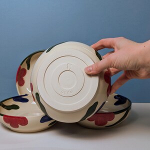 Pode incluir: Tr&ecirc;s tigelas de cer&acirc;mica com fundo branco e um design floral em vermelho, verde e azul. As tigelas est&atilde;o empilhadas umas sobre as outras. A tigela inferior tem a palavra "OCOCO" estampada na parte inferior.