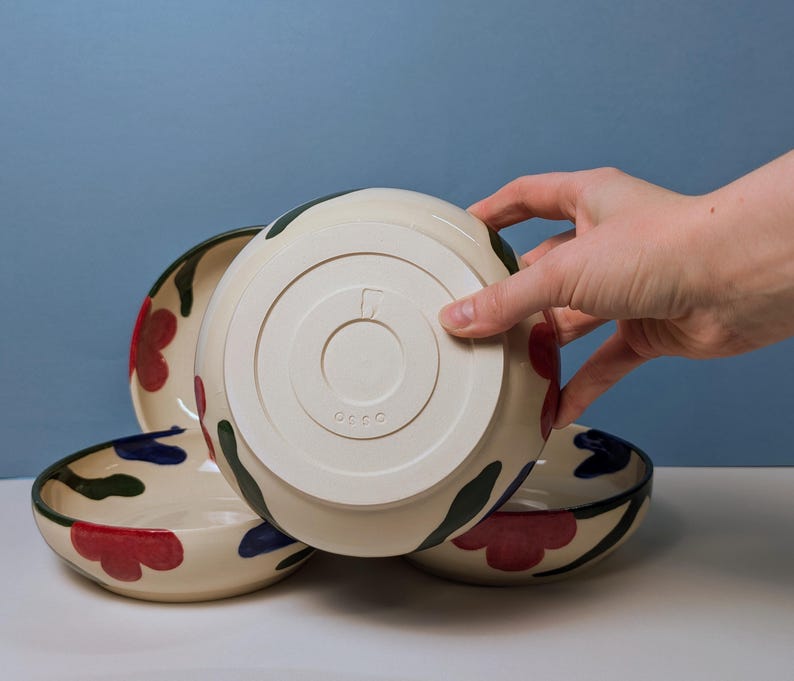 Pode incluir: Tr&ecirc;s tigelas de cer&acirc;mica com fundo branco e um design floral em vermelho, verde e azul. As tigelas est&atilde;o empilhadas umas sobre as outras. A tigela inferior tem a palavra "OCOCO" estampada na parte inferior.
