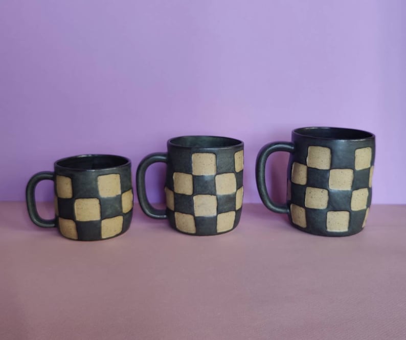Puede incluir: Tres tazas de cer&aacute;mica con un patr&oacute;n de cuadros en negro y marr&oacute;n. Las tazas son de diferentes tama&ntilde;os.