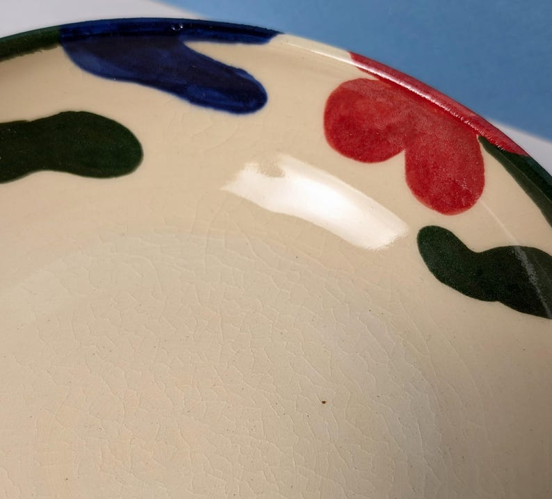 Pode incluir: Uma tigela de cer&acirc;mica branca com um esmalte craquelado. A tigela tem um design abstrato colorido com formas verdes, azuis e vermelhas.