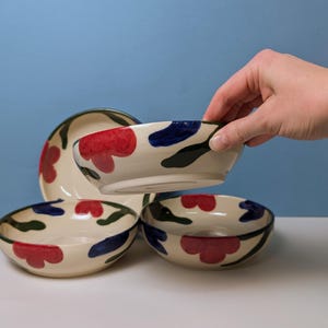 Pode incluir: Quatro tigelas de cer&acirc;mica com fundo branco e desenhos florais abstratos em vermelho, azul e verde. As tigelas est&atilde;o empilhadas umas sobre as outras.