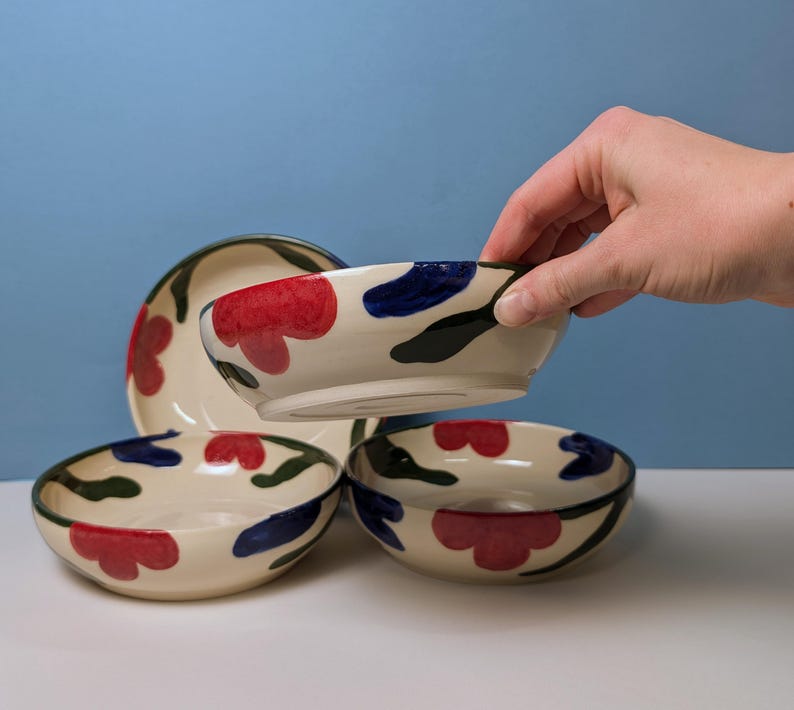 Pode incluir: Quatro tigelas de cer&acirc;mica com fundo branco e desenhos florais abstratos em vermelho, azul e verde. As tigelas est&atilde;o empilhadas umas sobre as outras.