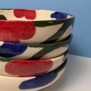 Pode incluir: Conjunto de quatro tigelas de cer&acirc;mica com base branca e desenhos abstratos em verde, vermelho e azul.