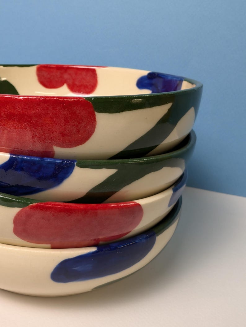 Pode incluir: Conjunto de quatro tigelas de cer&acirc;mica com base branca e desenhos abstratos em verde, vermelho e azul.