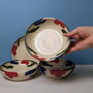 Pode incluir: Conjunto de quatro tigelas de cer&acirc;mica com fundo branco e um padr&atilde;o floral em vermelho, azul e verde.
