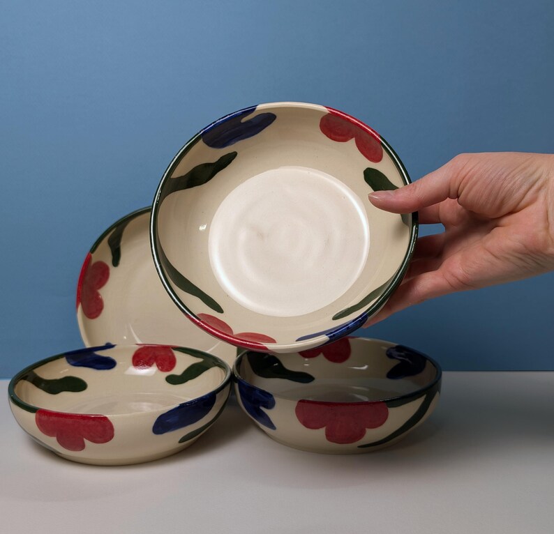 Pode incluir: Conjunto de quatro tigelas de cer&acirc;mica com fundo branco e um padr&atilde;o floral em vermelho, azul e verde.