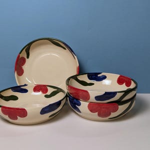 Pode incluir: Conjunto de quatro tigelas de cer&acirc;mica branca com um design floral verde, azul e vermelho.