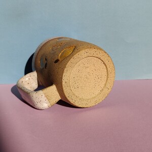 May include: A speckled brown and white ceramic mug with a white handle. The mug has a speckled brown glaze and a white rim.
