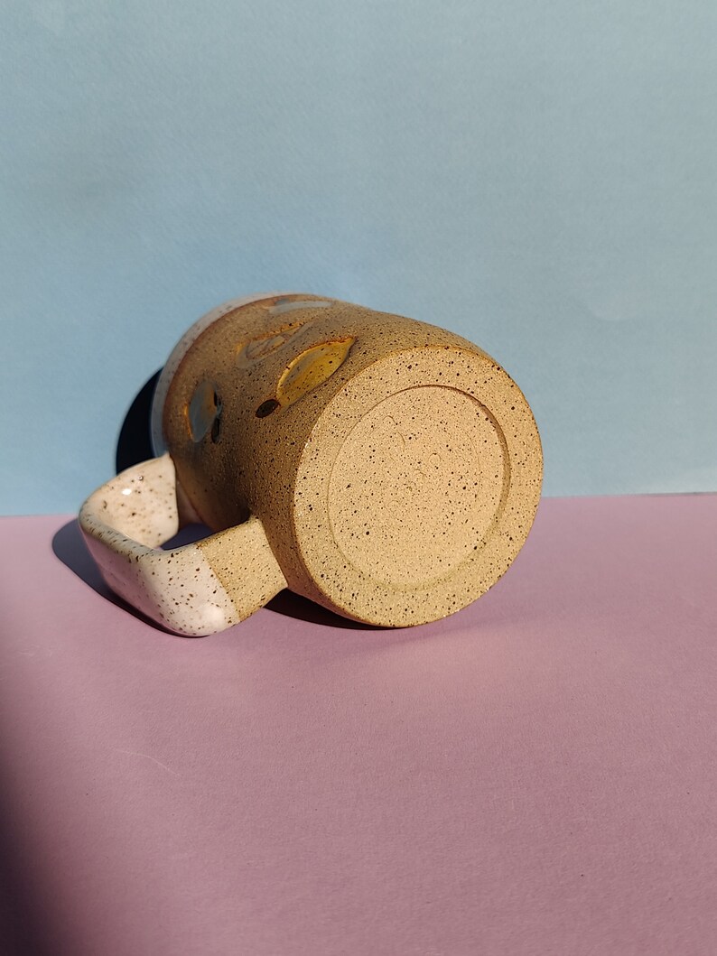 May include: A speckled brown and white ceramic mug with a white handle. The mug has a speckled brown glaze and a white rim.