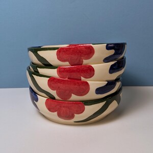 Pode incluir: Pilha de quatro tigelas de cer&acirc;mica branca com um design floral verde, azul e vermelho.