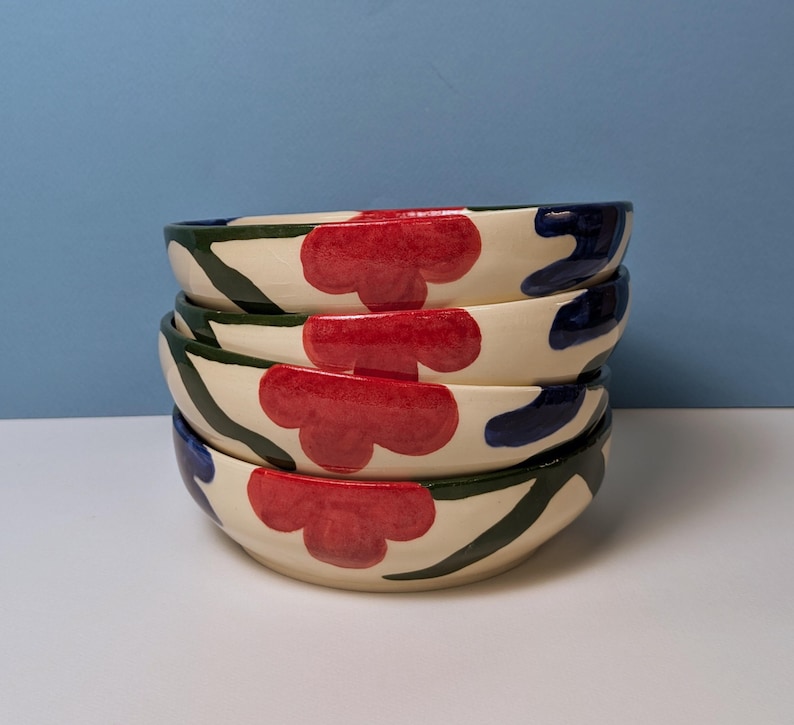 Pode incluir: Pilha de quatro tigelas de cer&acirc;mica branca com um design floral verde, azul e vermelho.