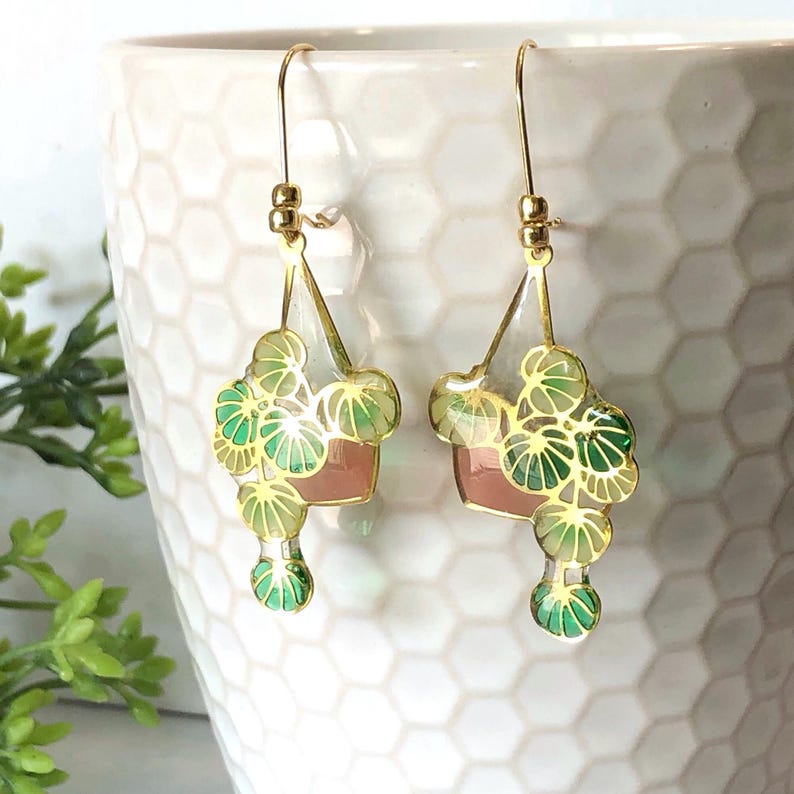 Puede incluir: Pendientes de aro dorados con un dise&ntilde;o floral rosa y verde. Los pendientes tienen forma de maceta peque&ntilde;a con una planta que sale de ella.