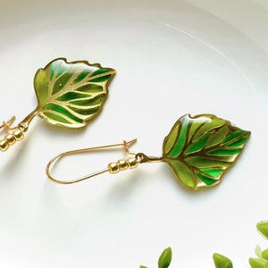 May include: A pair of gold leaf earrings with green and gold enamel. The leaves are detailed with a delicate vein pattern.