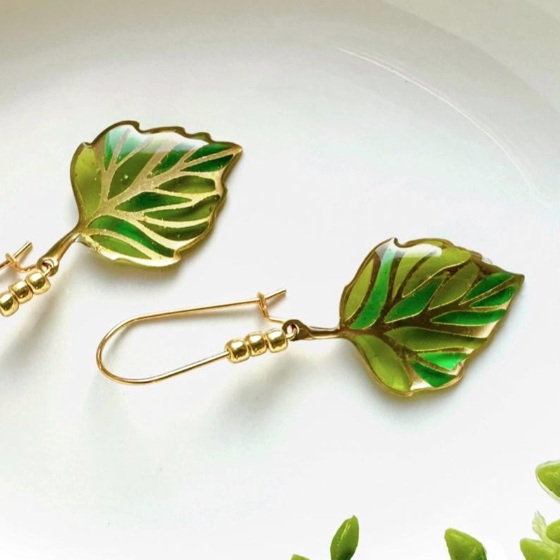 May include: A pair of gold leaf earrings with green and gold enamel. The leaves are detailed with a delicate vein pattern.