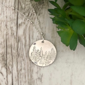 May include: A silver necklace with a round pendant featuring an etched design of a forest with trees.