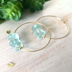 May include: Gold hoop earrings with light blue glass beads. The beads are stacked on the hoop.