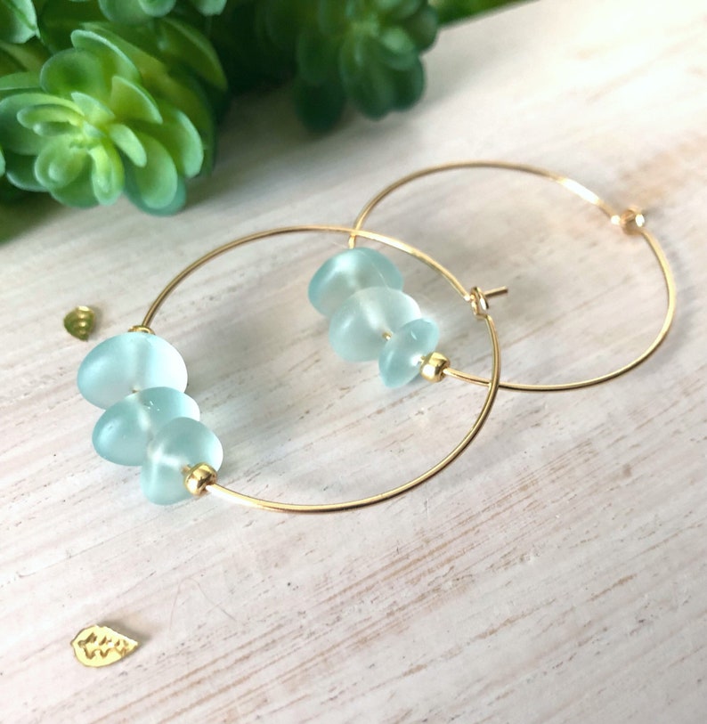 May include: Gold hoop earrings with light blue glass beads. The beads are stacked on the hoop.