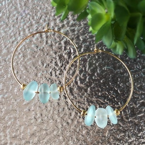 May include: A pair of gold hoop earrings with three light blue glass beads on each hoop.