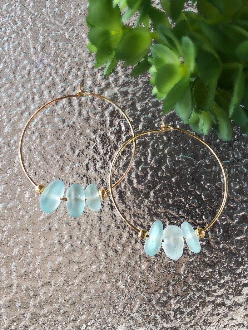 May include: A pair of gold hoop earrings with three light blue glass beads on each hoop.