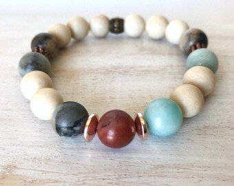 May include: A beaded bracelet featuring a mix of natural stones, including white, brown, grey, green, and red beads. The bracelet has copper accents and a copper clasp.