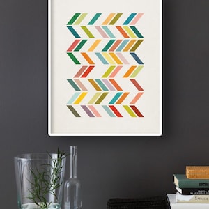 May include: A framed print with a geometric pattern of colorful chevron shapes on a white background. The print is hanging on a dark gray wall.