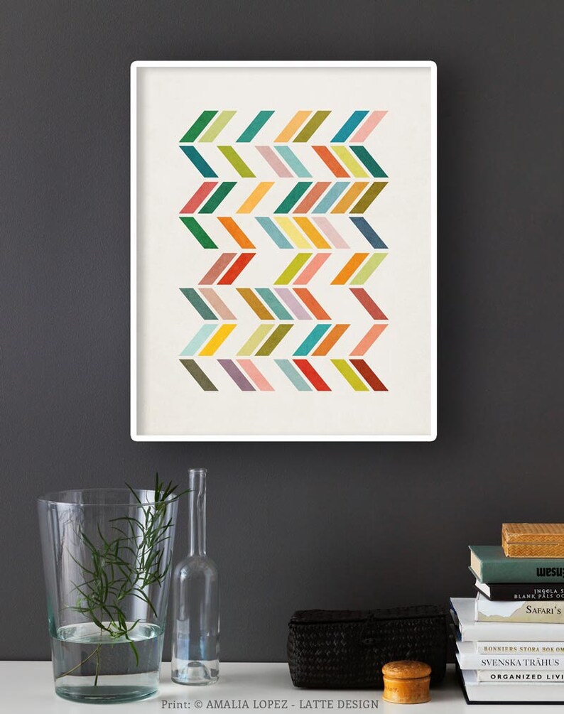 May include: A framed print with a geometric pattern of colorful chevron shapes on a white background. The print is hanging on a dark gray wall.