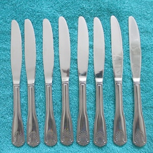 May include: Eight silver dinner knives with ornate handles on a turquoise blue towel.